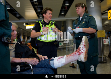 NHS paramedico i soccorritori assiste una signora passeggero a Heathrow il terminale 3 che ha scattato e mal tagliato profondamente la sua gamba. Foto Stock