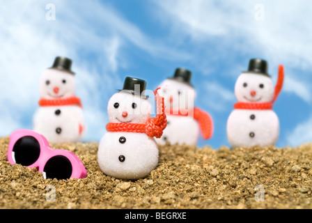 Natale ornamenti ai pupazzi di neve su una spiaggia di ghiaia con occhiali da sole rosa per eseguire il cast di un estate tropicale tema. Foto Stock