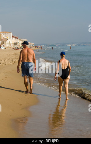 Coppia di anziani Beachwear passeggiando lungo la spiaggia vista da dietro Foto Stock