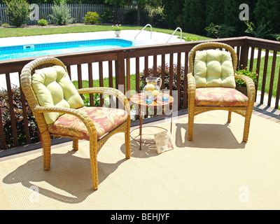 Due comode sedie su un patio che si affaccia su una piscina nel giardino di casa Foto Stock