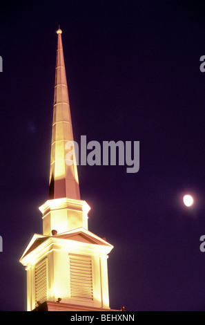 Church steeple lit for evening services in cold winter night with moon rising Vermont USA Foto Stock