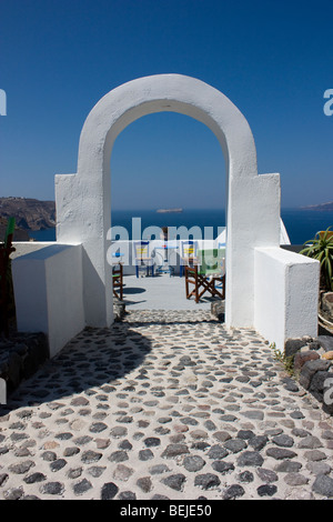 Tipicamente bella, bianco arch, fiori di colore rosa e sedie blu, Santorini, Grecia Foto Stock