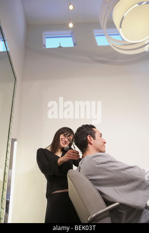 Basso angolo vista di una femmina di parrucchiere a parlare su un telefono cordless e il taglio di capelli di una metà di uomo adulto Foto Stock