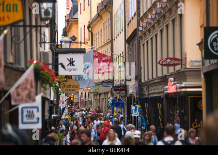 La folla degli acquirenti shopping sotto i segni sulla trafficata strada turistica Västerlånggatan nella città vecchia di Stoccolma, la Gamla Stan. Foto Stock