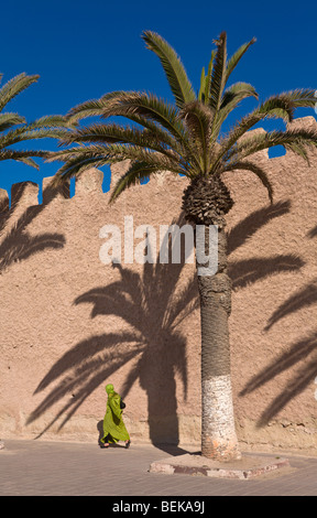 Donna locale camminando accanto alla cinta muraria della città essaouira marocco Foto Stock