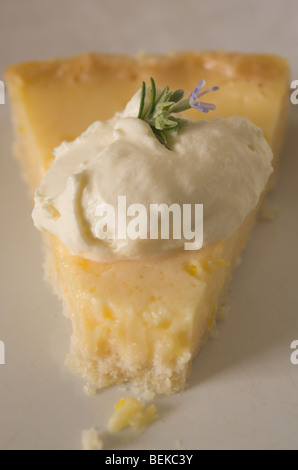Un parzialmente mangiato fetta di limone fatti in casa crostata con panna montata e decorate con un fiore di rosmarino Foto Stock