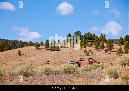 Una vecchia ruggine auto sconosciuto di marca e modello si siede la formazione di ruggine sulle colline di miniere d'oro città fantasma di Elizabethtown, NM Foto Stock