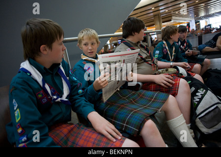 Ragazzi da un scozzese gruppo scout sedersi e nell'atrio partenze dell'aeroporto di Heathrow il Terminal 5. Foto Stock