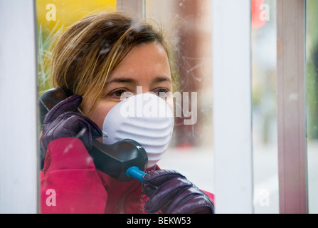 Donna che indossa la maschera a parlare su un telefono pubblico Foto Stock