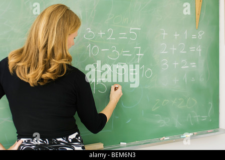 Insegnante elementare aritmetica di scrittura sulla lavagna, vista posteriore Foto Stock