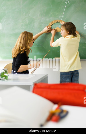 Insegnante che mostra degli studenti elementari come disegnare un angolo tramite goniometro Foto Stock