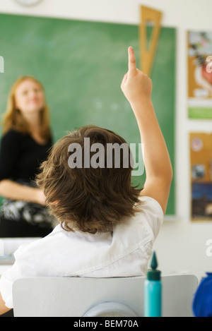Studente elementare alzando la mano in classe, vista posteriore Foto Stock