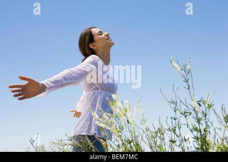 Giovane donna in piedi in erba alta con braccia a occhi chiusi Foto Stock