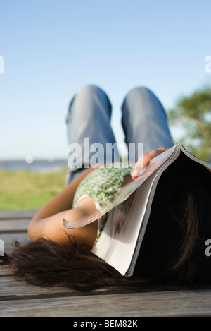 Donna sdraiata sul dock con la rivista che copre il volto Foto Stock