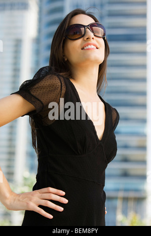 Donna vestito in abiti neri e occhiali da sole, guardando verso l'alto e sorridente Foto Stock