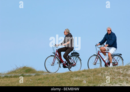 Anziani ciclisti su biciclette Maneggio nelle dune lungo la costa del Mare del Nord Foto Stock