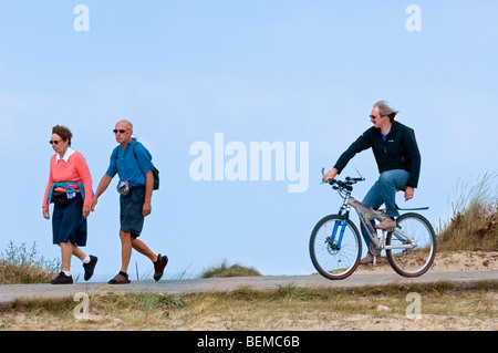 Ciclista e coppia di anziani a piedi nelle dune lungo la costa del Mare del Nord Foto Stock