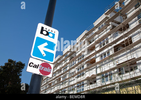 Un basso angolo di vista di BART e Caltrain cartelli stradali da un condominio scaffolded. Millbrae, California, Stati Uniti d'America Foto Stock