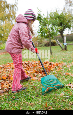Bambina colorata rake caduto foglie di autunno in giardino Foto Stock