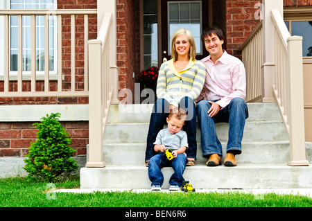 Famiglia giovane seduto sulla parte anteriore passi di casa Foto Stock