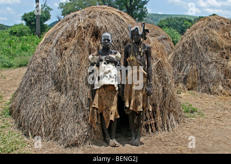 Due ragazze della tribù dei Mursi in abito tradizionale in posa di fronte della capanna in villaggio nella valle dell'Omo, Etiopia, Africa orientale Foto Stock