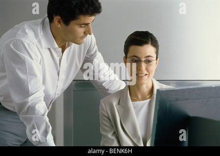 Giovani professionisti donna sorridente, guardando lo schermo del computer mentre il collega di sesso maschile si appoggia sulla sua spalla Foto Stock