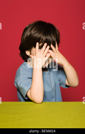 Little Boy che ricopre la faccia con le mani, spiata attraverso le dita in telecamera Foto Stock