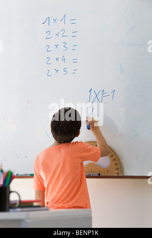 Scuola elementare studente facendo equazione matematica su whiteboard, vista posteriore Foto Stock