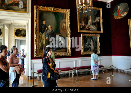 Francia - Piccola folla di turisti visita gli interni del castello francese, "Castello di Versailles", donne in una galleria d'arte, ascoltando guide audio turistiche Foto Stock