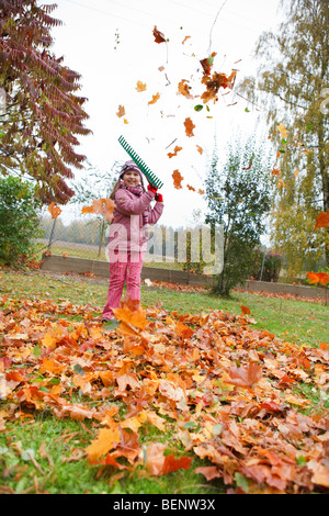 Bambina colorata rake caduto foglie di autunno in giardino Foto Stock