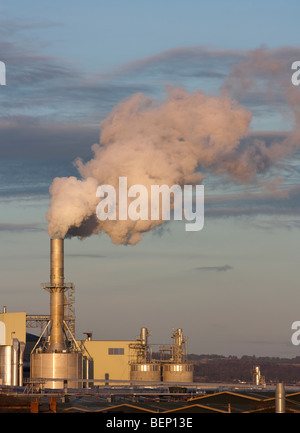 Impianto industriale impostato in area rurale produca grandi nuvole di vapore o fumo inquinamento sotto un sole di setting. Foto Stock