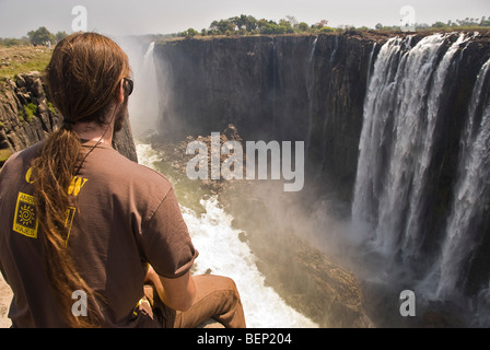 L'uomo guarda il Victoria falls seduto sul bordo, Zimbabwe, Africa. Foto Stock