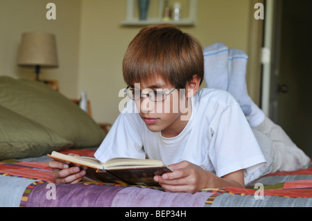 Un giovane bambino ragazzo a leggere un libro sul suo letto Foto Stock