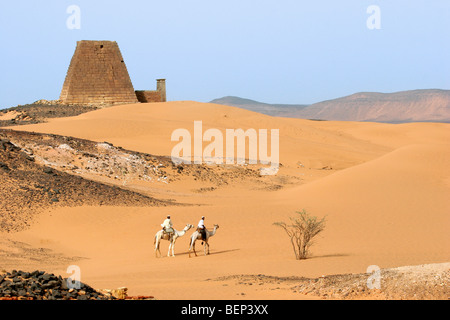 Piramidi di Meroe e due Nubian uomini vestiti in thawbs cavalcare dromedari nel deserto nubiano sudanese, Nord Africa Foto Stock