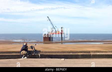 Uomo con bicicletta guardando pipeline piattaforma di riparazione sulla spiaggia Foto Stock