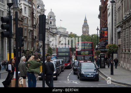 Scena di strada, visualizza in basso Whitehall verso il Big Ben da Trafalgar Square. Un giovane uomo si appoggia sul controllo di attraversamento Foto Stock