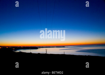 Due piccole barche con bassa marea si stagliano contro la luce del sole scintillante sull'acqua, con la costa e edifici distanti sullo sfondo. An nero Foto Stock