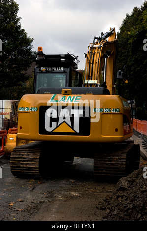 Escavatore cingolato in Crouch Hill , Londra Nord visto in uso resurfacing la strada presso la fermata del bus area. Foto Stock