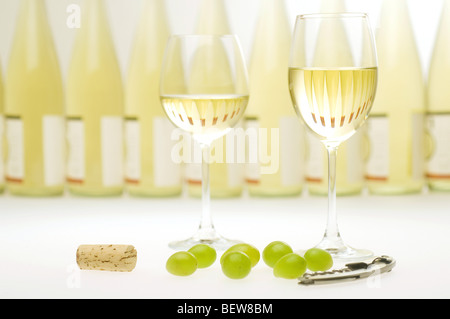 Riempito due calici da bianco nella parte anteriore di una fila di bottiglie di vino, still life Foto Stock