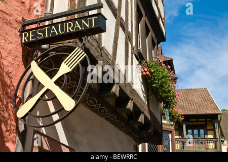 Alsazia Ristorante segno di attraversato il coltello e forchetta con tipico soleggiato Alsazia floreali case in Francia di sfondo Foto Stock