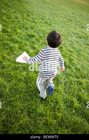 Tre anni di vecchio ragazzo giapponese corre attraverso un parco che porta il suo aeroplano di carta Foto Stock