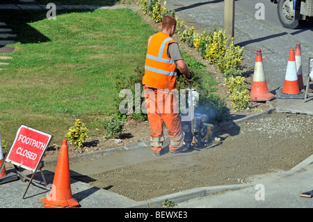 Operai frequentando il marciapiede marciapiede di riparazioni in strada residenziale Foto Stock