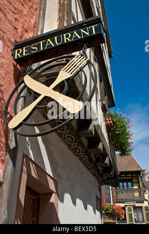 Alsazia ristorante Francese e segno di attraversato il coltello e forchetta con tipico soleggiato Alsazia floreali case in Francia di sfondo Foto Stock