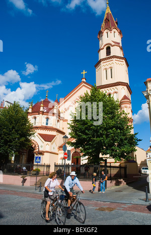 Coppia di mezza età equitazione biciclette passato la chiesa di San Nicola nella città vecchia di Vilnius Lituania Europa Foto Stock