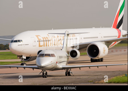 Emirates Airlines Boeing 777-31il suo aereo di linea A6-BCE rullaggio dietro Canadair Challenger 600 VP-CFT all'Aeroporto di Manchester Inghilterra England Foto Stock