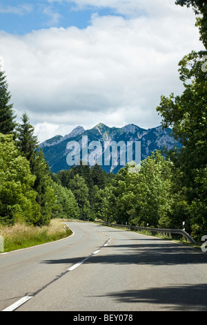 Viaggiando lungo una strada aperta attraverso il bosco verso le montagne in Baviera Germania Europa Foto Stock