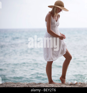 Giovane donna con cappello di paglia in piedi di fronte al mare Foto Stock