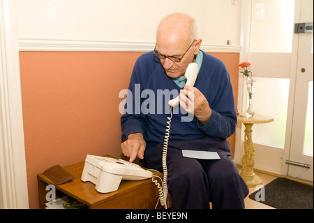 Un uomo anziano nella sua casa di comporre un numero sul suo telefono Foto Stock