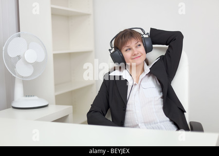 La donna si siede in una poltrona e ascolta la musica in grande auricolari Foto Stock