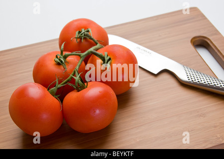 Organici di pomodori a grappolo con coltello da cucina in bambù tagliere Foto Stock